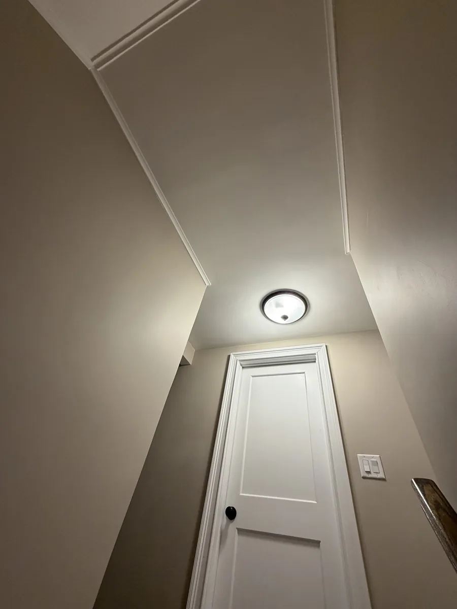 Completed hallway and stairwell with smooth painted ceiling, neutral walls and white door trim