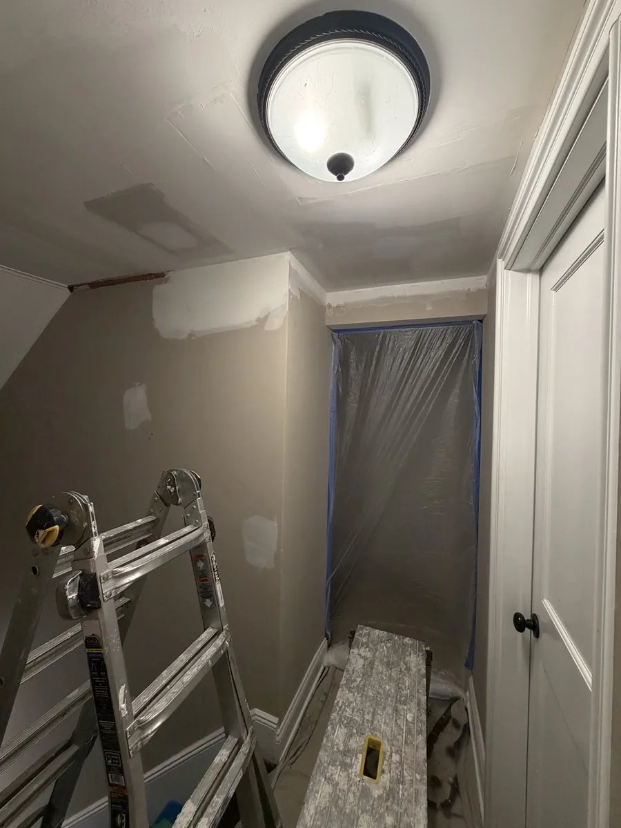 Hallway ceiling patching and surface preparation in progress with drop cloths installed