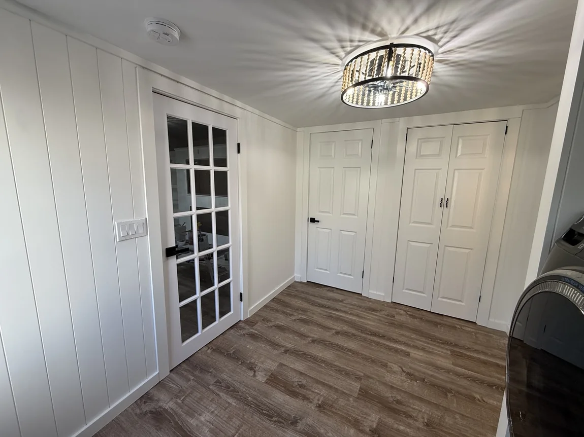 Finished laundry room with white panel walls, white doors, black accent, and washer dryer